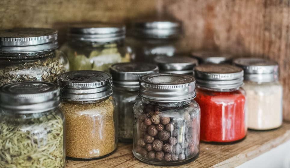 An array of colorful spices and seasonings arranged in jars on a wooden shelf.